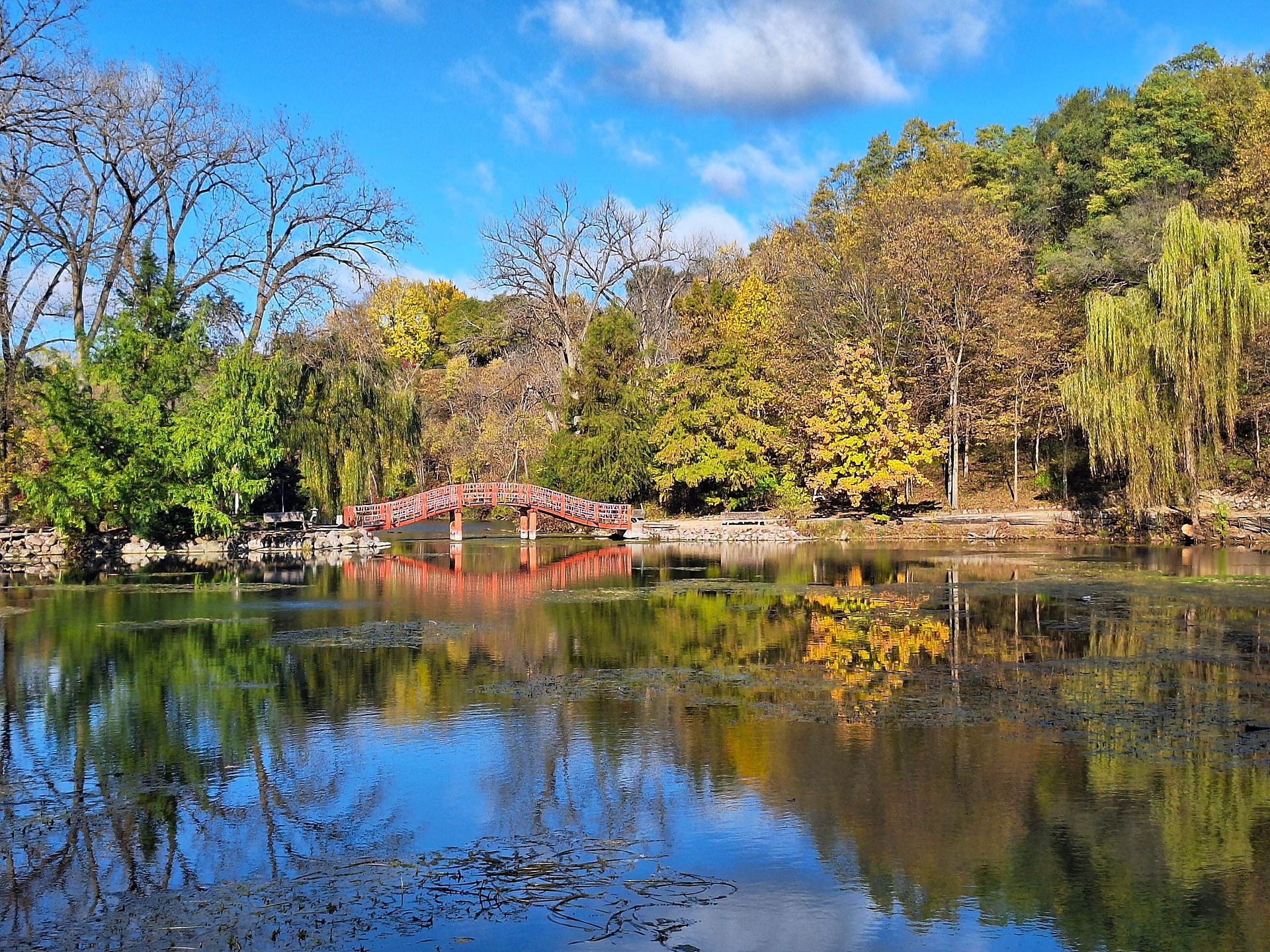 Red bridge reflected in pond surrounded by fall trees.