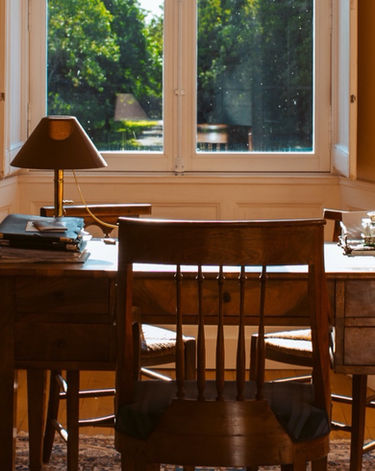 A well-lit study space featuring a wooden desk and chair with a lamp and a window.