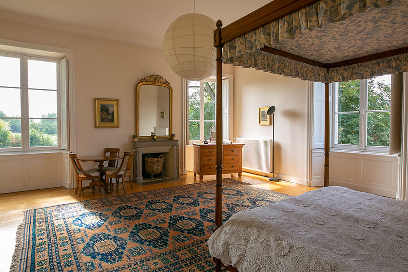 Spacious and bright master bedroom in the chateau with king size four poster bed, large rug, and wooden parquet floors.