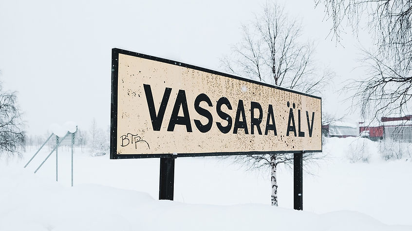 Sliten gultblekt skylt bredvid strandkanten, med texten VASSARA ÄLV.