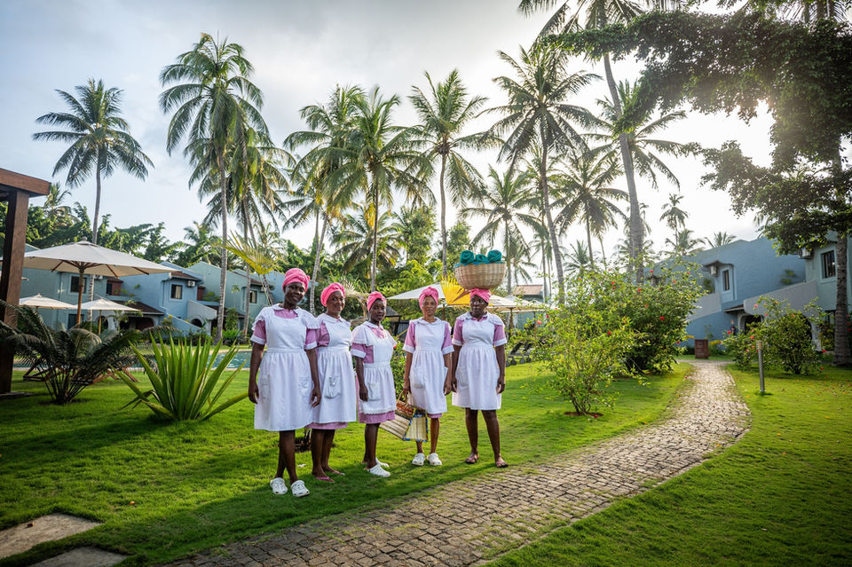 Five women in white uniforms stand in a tropical garden.