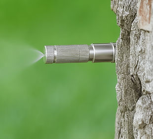 Mosquito misting nozzle spraying beside a tree trunk