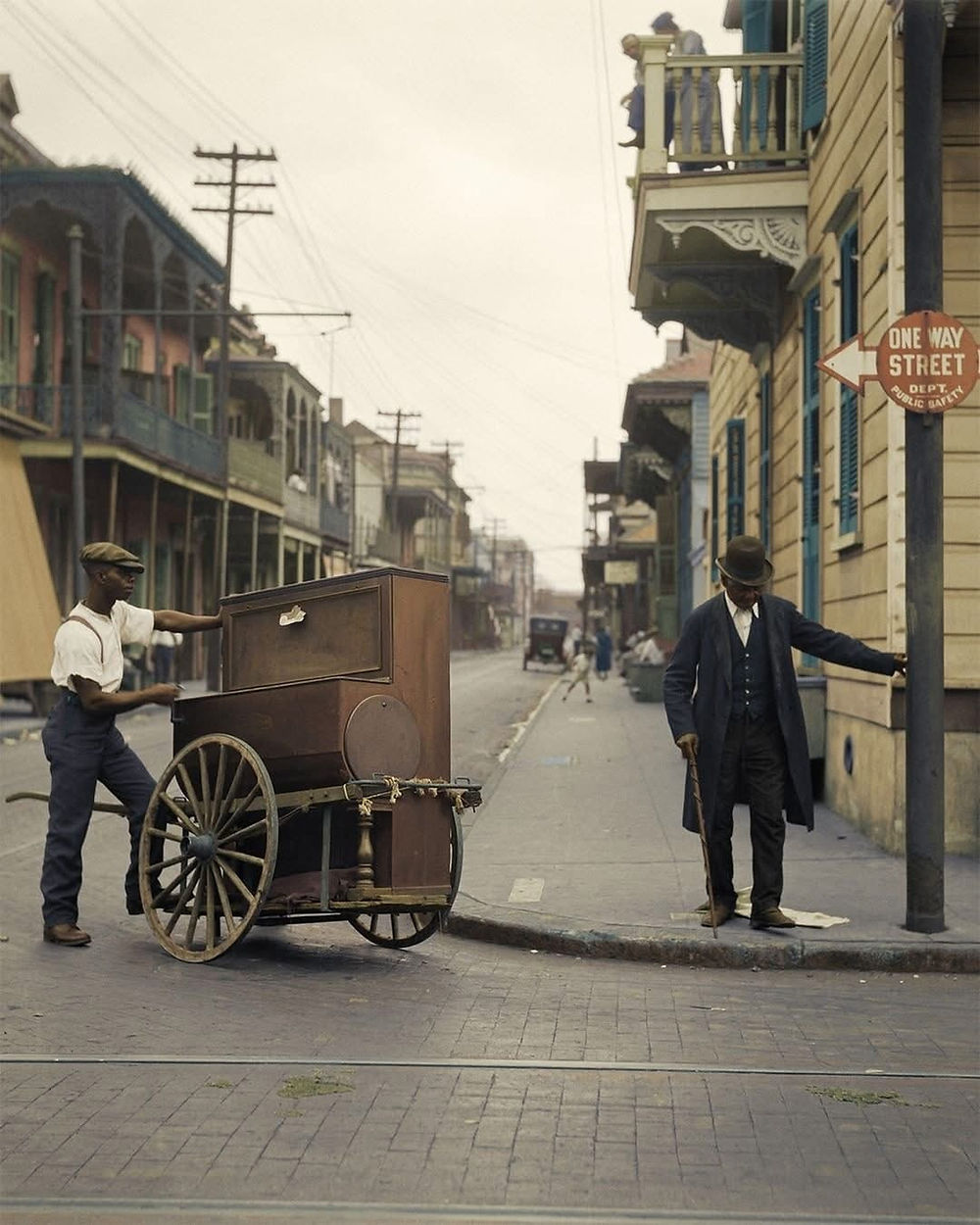 Man pulling a piano on a cart in a historic street.