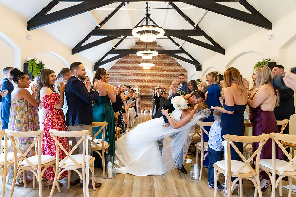 Wedding couple kiss in an aisle as guests applaud.