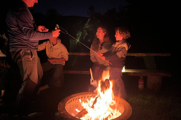 A man helping a boy toast a marshmallow by a campfire