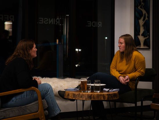two women sitting in chairs at a table with drinks on it