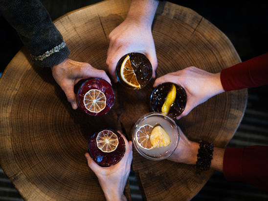 Five drinks being held in a circle on a wooden table