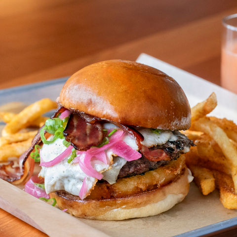 A burger with red onions, egg, bacon and fries. a drink is in the background. Brunch menu by Cody Pratt at Madbush Falls, Waitsfield, Vermont.