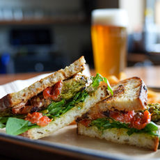 chicken sandwich with greens, chimichurri and fries with a beer. Lunch menu by Cody Pratt at Madbush Falls, Waitsfield, Vermont.