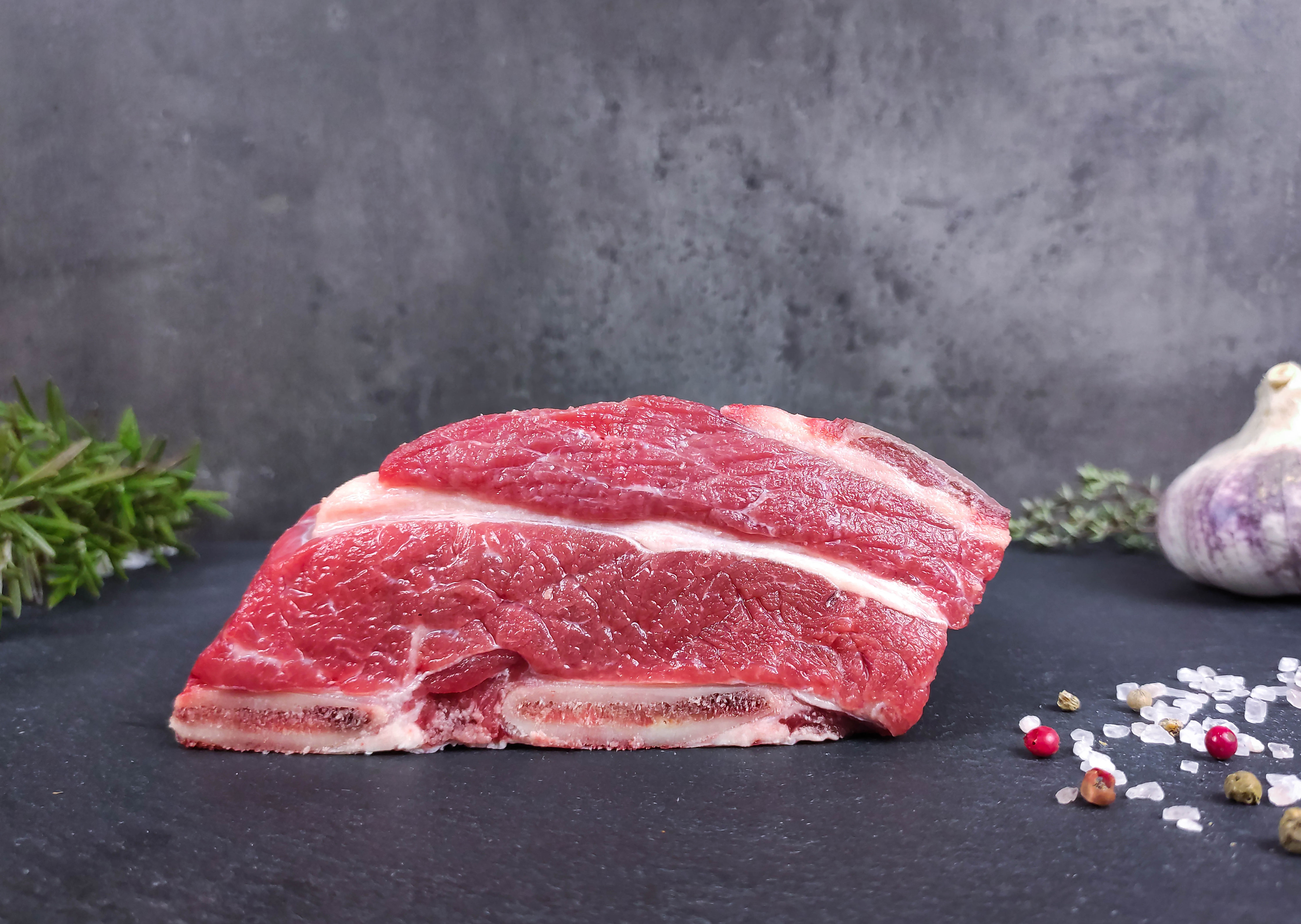 Ein zartes Stück Biofleisch umgeben von Kräutern und Gewürzen liegt auf einer dunklen Schieferplatte.