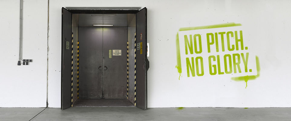 Ein geöffneter schwarzer Aufzug. Rechts daneben ein Schriftzug: NO PITCH. NO GLORY.