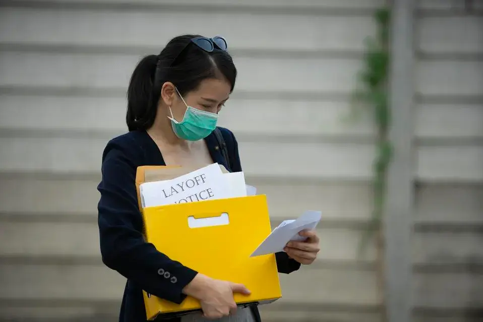 Woman holding a yellow folder and a paper that reads, "Layoff notice."