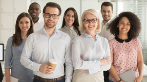 A group of seven people from diverse backgrounds smiling in an office setting
