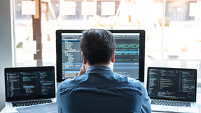 Person coding on multiple computer screens in a modern office setting.