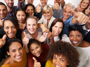 A diverse group of smiling people giving thumbs-up gestures indoors.