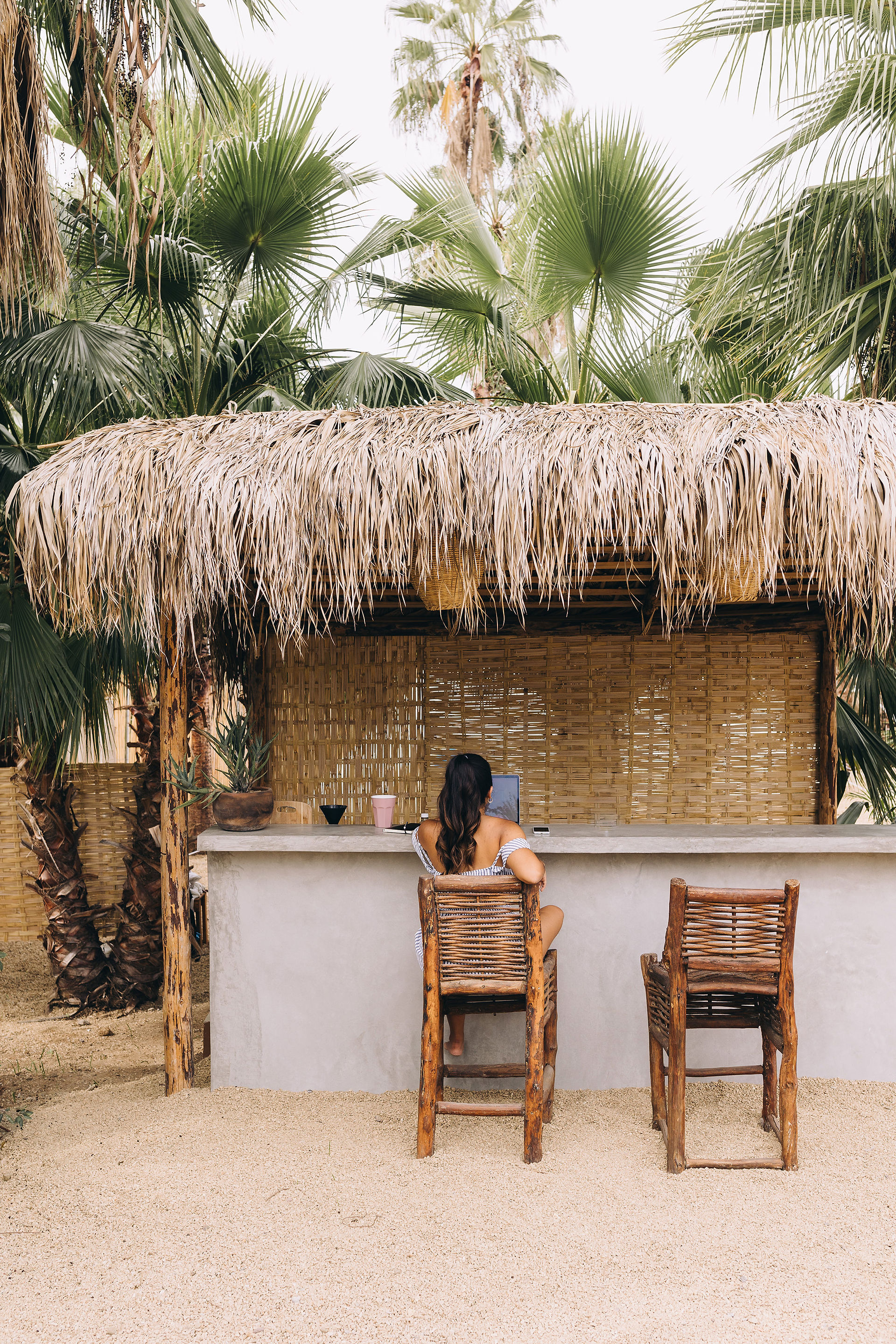 Woman sits at rustic counter beach bar counter top on her laptop