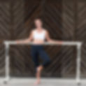 Christine in a white top and black leggings posing for a photo next to a barre