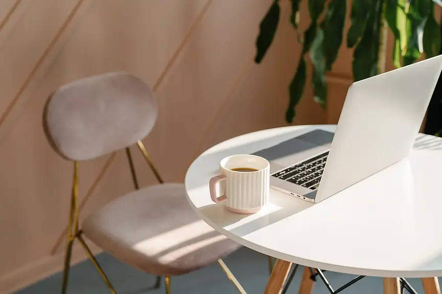 laptop open on a desk with a mug and dusty pink chair