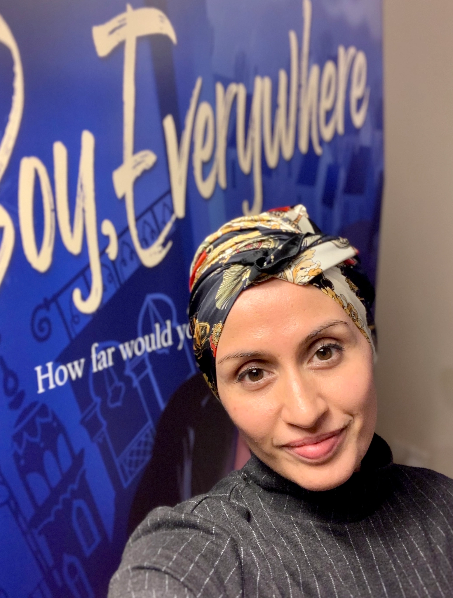 AM Dassu standing in front of poster of her book Boy, Everywhere