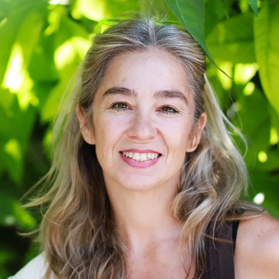 Portrait of Alkista Halikia, smiling outdoors in front of green leaves.