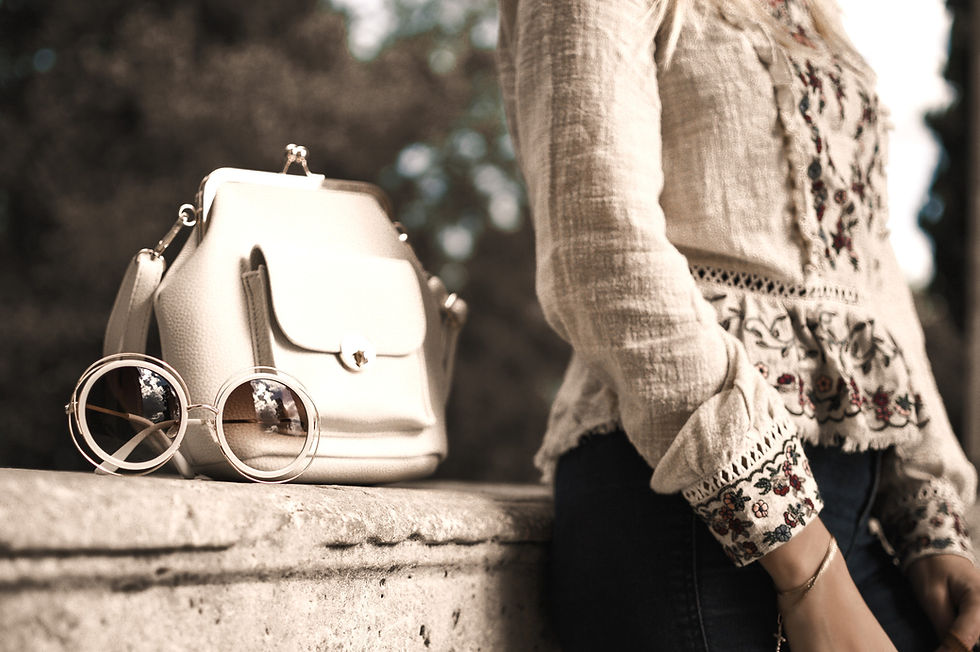 Sepia image of woman leaning against a wall with her sunglasses and handbag