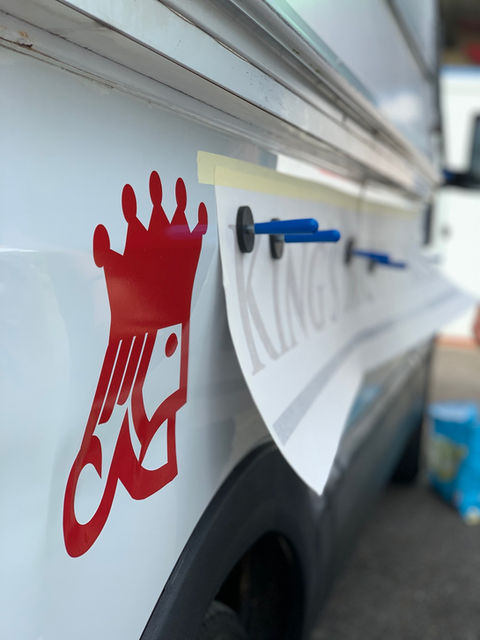 Vinyl graphics in production - application of red King's Brothers logo across side of white van. 