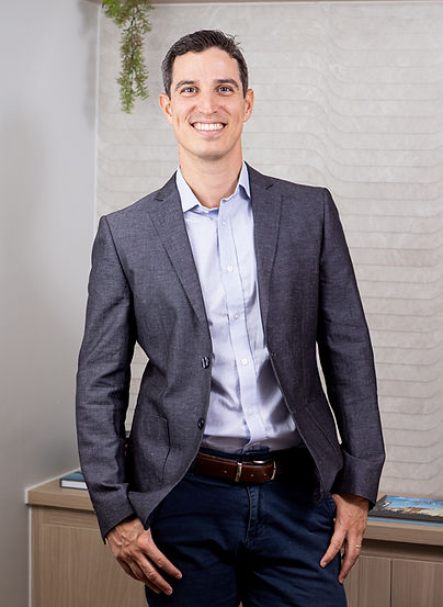 Dr. Eutímio Aires Brasil sorrindo, vestindo terno escuro com camisa clara, em frente a fundo branco.