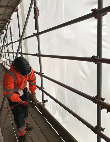 Trainer demonstrating heat-welding of shrink wrap sheeting on scaffolding