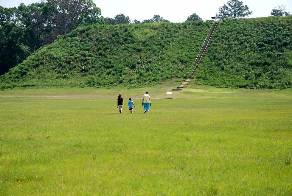A family walking across an open green field toward the great temple mound at Kolomoki Mounds State Park near Blakely, Georgia