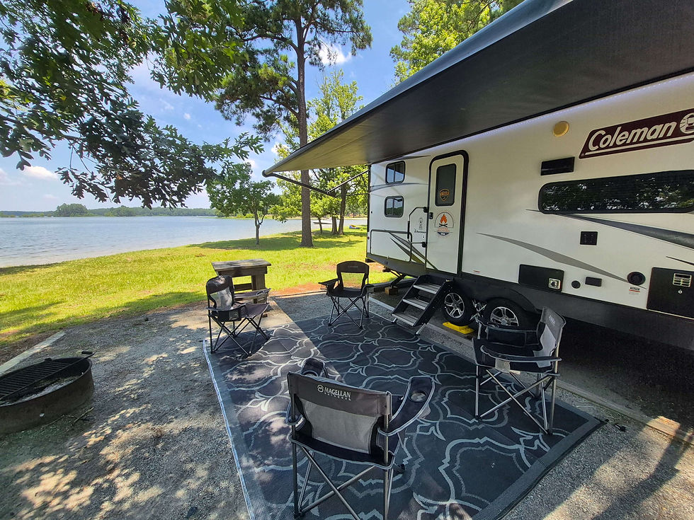 Willie, a Campfire Adventures Coleman travel trailer, fully set up with awning, camp chairs, and outdoor rug at a lakeside campsite on Lake Walter F. George (Lake Eufaula) in Southwest Georgia.