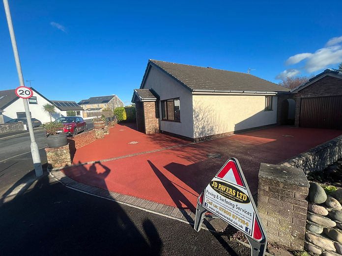 A single-story house with a red paved driveway is seen on a sunny day