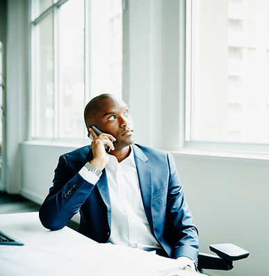 Businessman on smartphone sitting at office desk looking out window