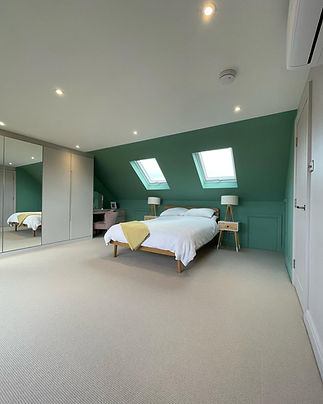 Spacious attic bedroom with green wall twin skylight windows and fitted wardrobes