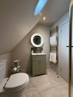 Compact en suite bathroom under sloped roof with circular mirror vanity unit and towel rail