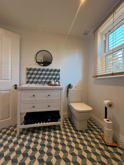 En suite bathroom interior showing circular wall mirror patterned tile splashback and window