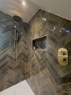 Close up of dark grey herringbone tiles with brass shower fixtures and recessed wall niche