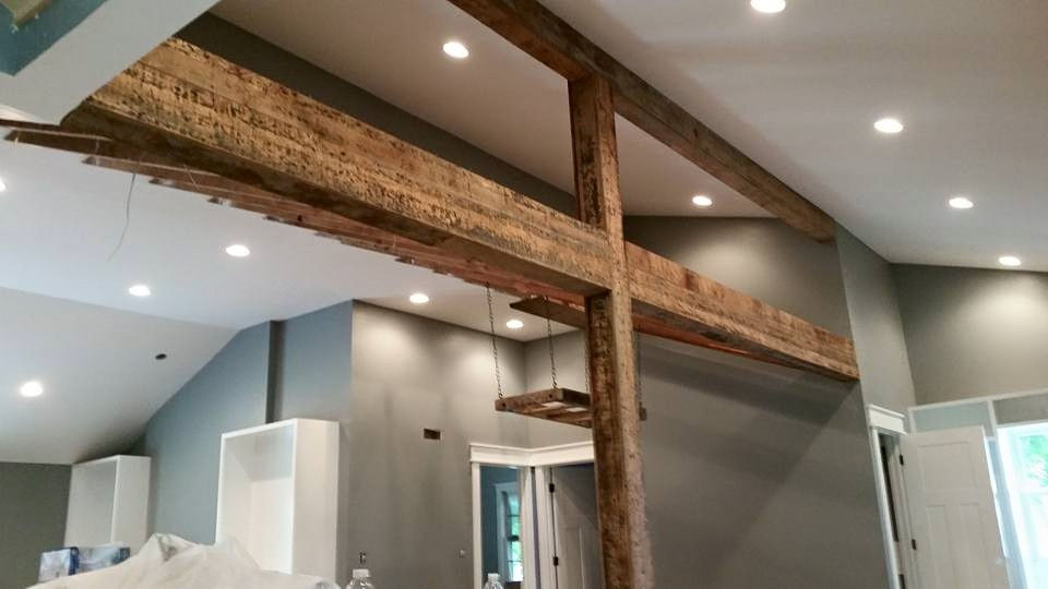 Rustic reclaimed wood beam wraps installed across a vaulted interior opening.