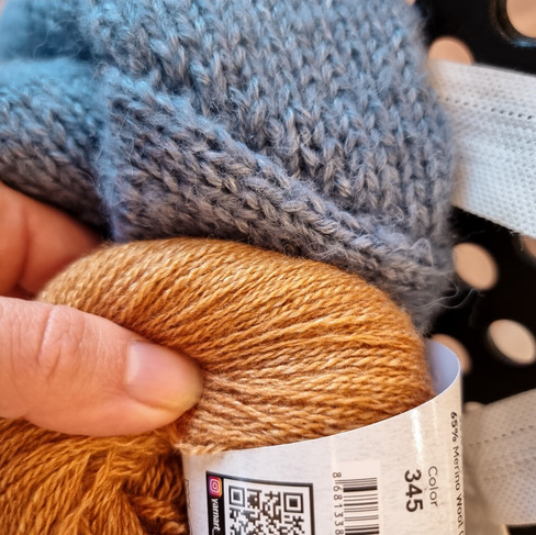 A golden tan yarn being held up to a periwinkle blue sweater for comparison