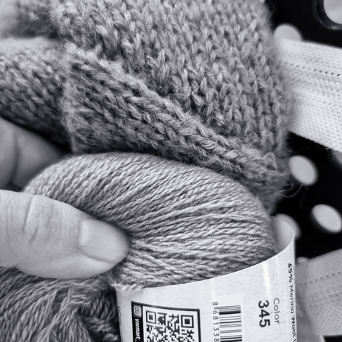 Black and white picture of yarn being held up to a knitted garment. They look like almost the exact same color.