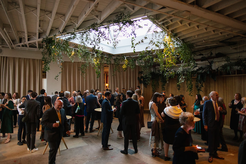 nyc wedding dj new york wedding timeline Guests in formal wear mingle at a lively indoor reception under hanging greenery and a bright skylight.