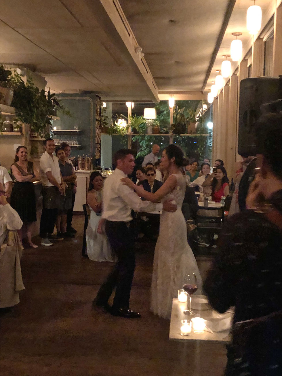 nyc wedding dj Bride and groom slow dance at a candlelit wedding reception, surrounded by smiling guests and greenery.