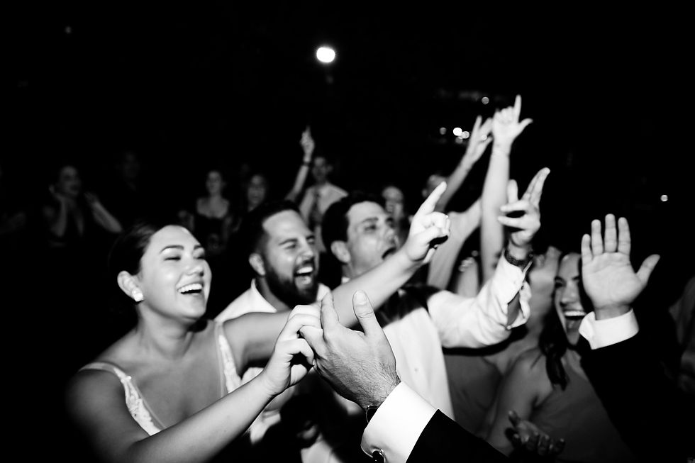 nyc wedding dj the william vale Black-and-white party crowd smiling and dancing, hands raised in a dark venue with bright lights in the background.
