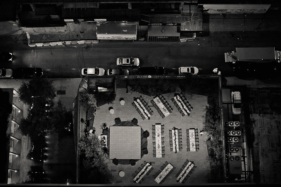 nyc wedding dj the william vale Aerial night view of a black-and-white rooftop dining setup beside a street with parked cars and trucks, quiet urban mood.