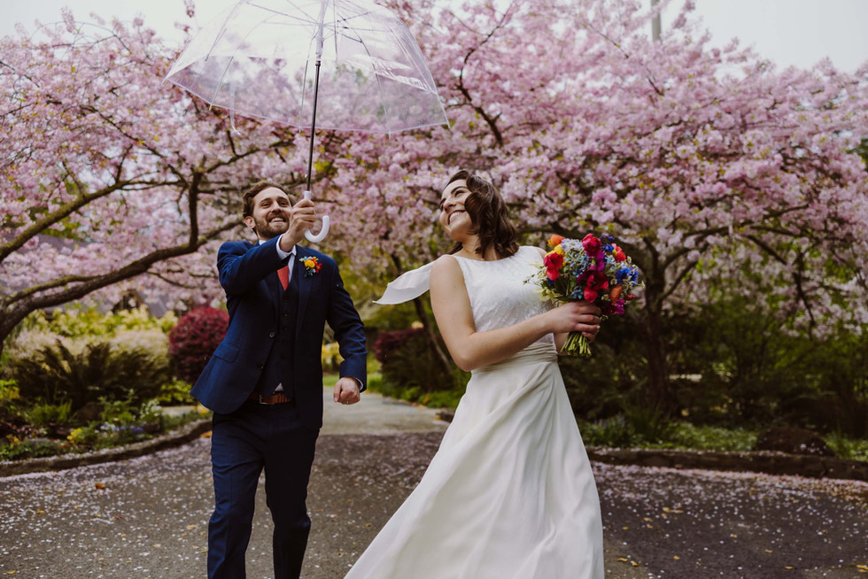 Bride and groom walking under cherry blossoms at the Brazilian Room in Berkeley, CA on a rainy wedding day