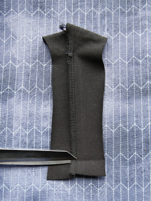 Close up view of an 3 thread overlocked seam in black jersey with scissors snipping the seam at the hemline