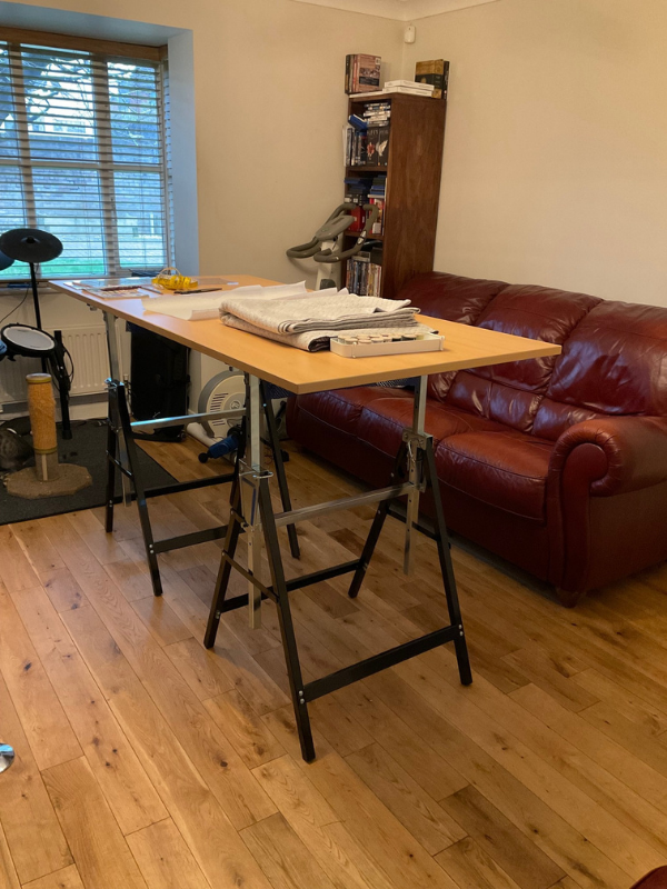 Large Ikea table top on two height adjustable metal trestles from Screwfix providing a large fabric cutting table and work surface for sewing, with height set at 1m