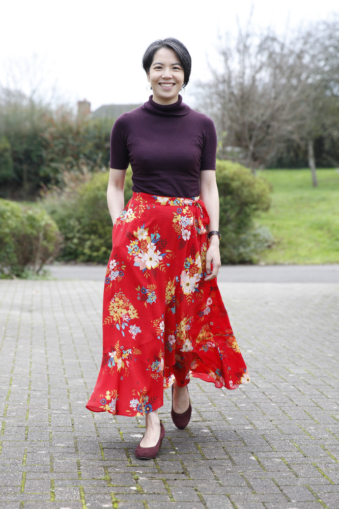 Young Asian female in Liberty Zina Wrap Skirt / Simplicity 8606 in a red floral rayon challis fabric. She is walking towards the camera, showing movement of the skirt