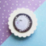 A round pocket mirror with an illustrated crying moon and stars. It sits on a white scallop, on a lilac and blue background.
