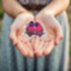 A colourful vinyl sticker of two lovebirds cuddling together, displayed in some hands.