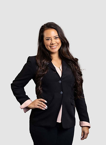 Carla Collins in a black suit posing, smiling, with hand on hip, looking at camera.